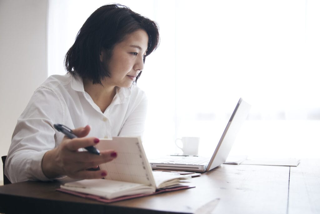 Japanese woman in casual clothes checking and writing the schedule on diary on the desk.
