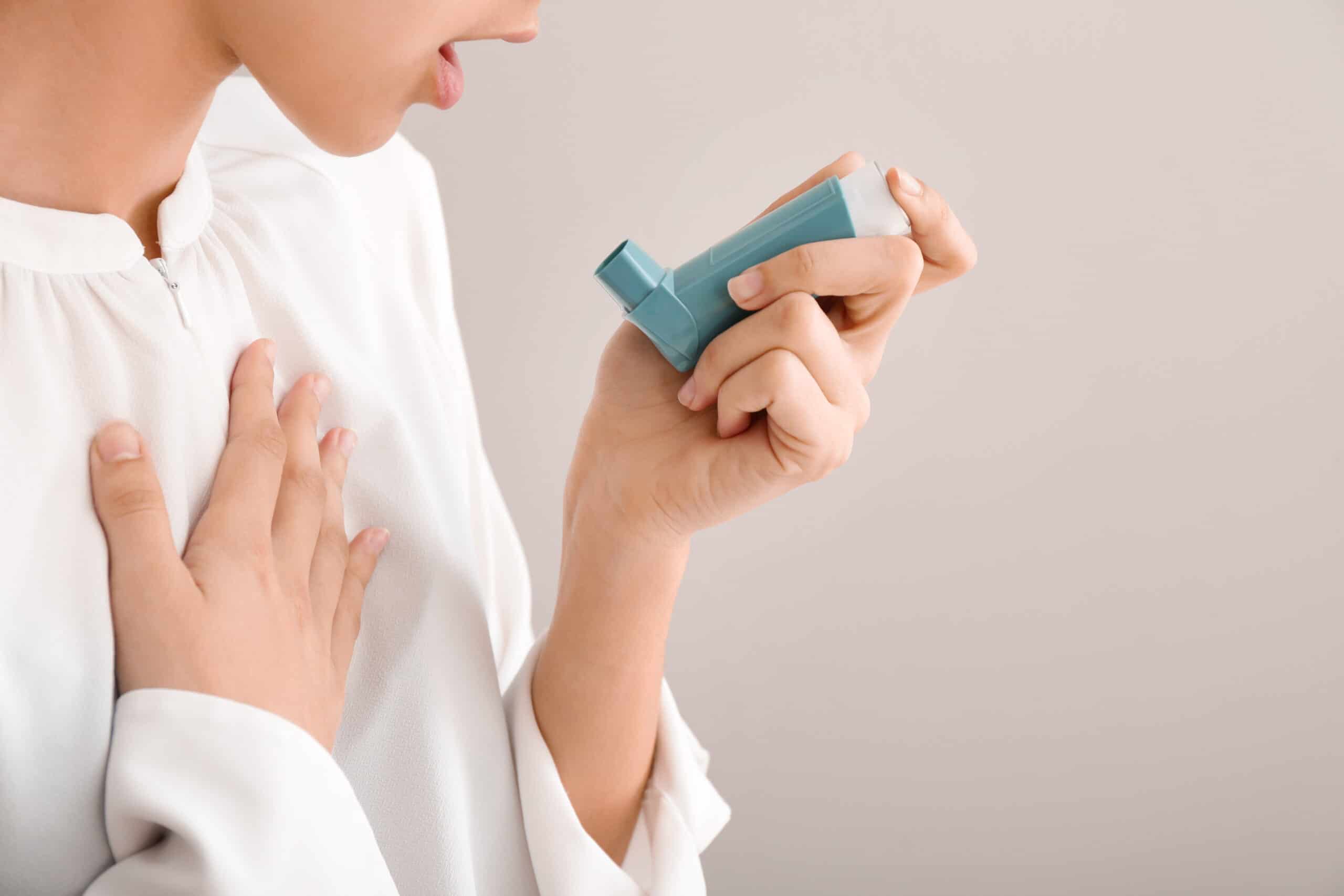 Young woman using inhaler against asthma on light background