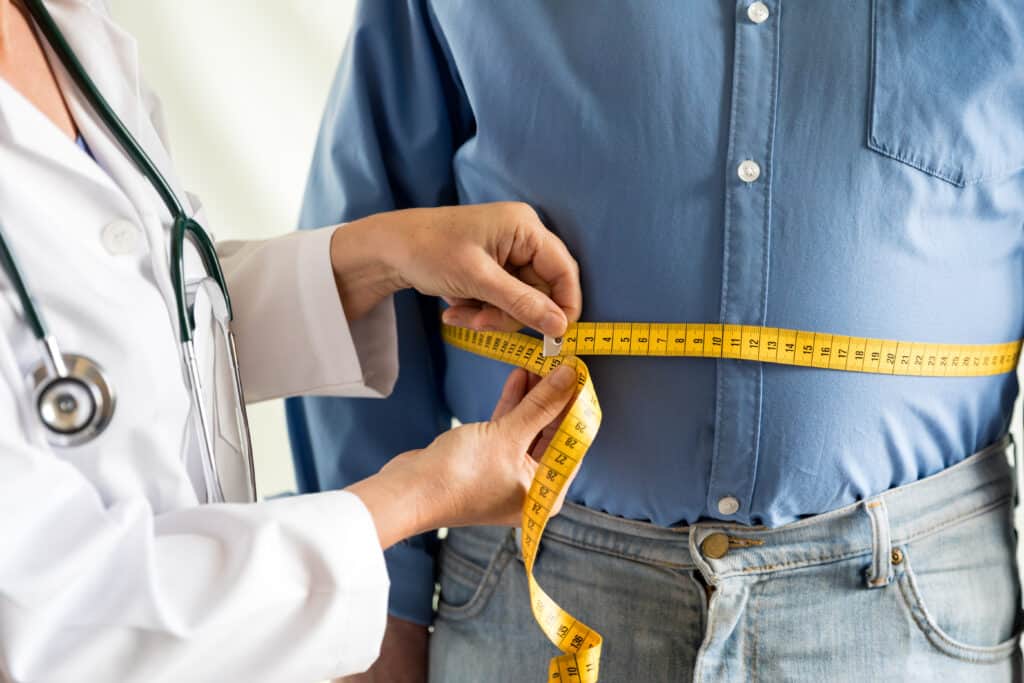 Overweight man getting waist measured by doctor