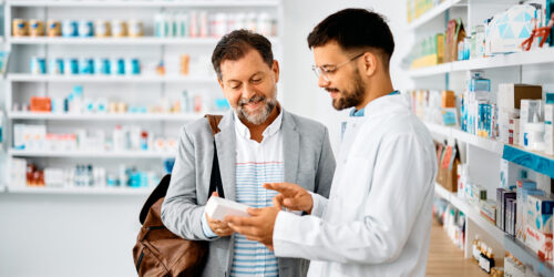 Happy man chooses medicine with help of young pharmacist in drugstore.