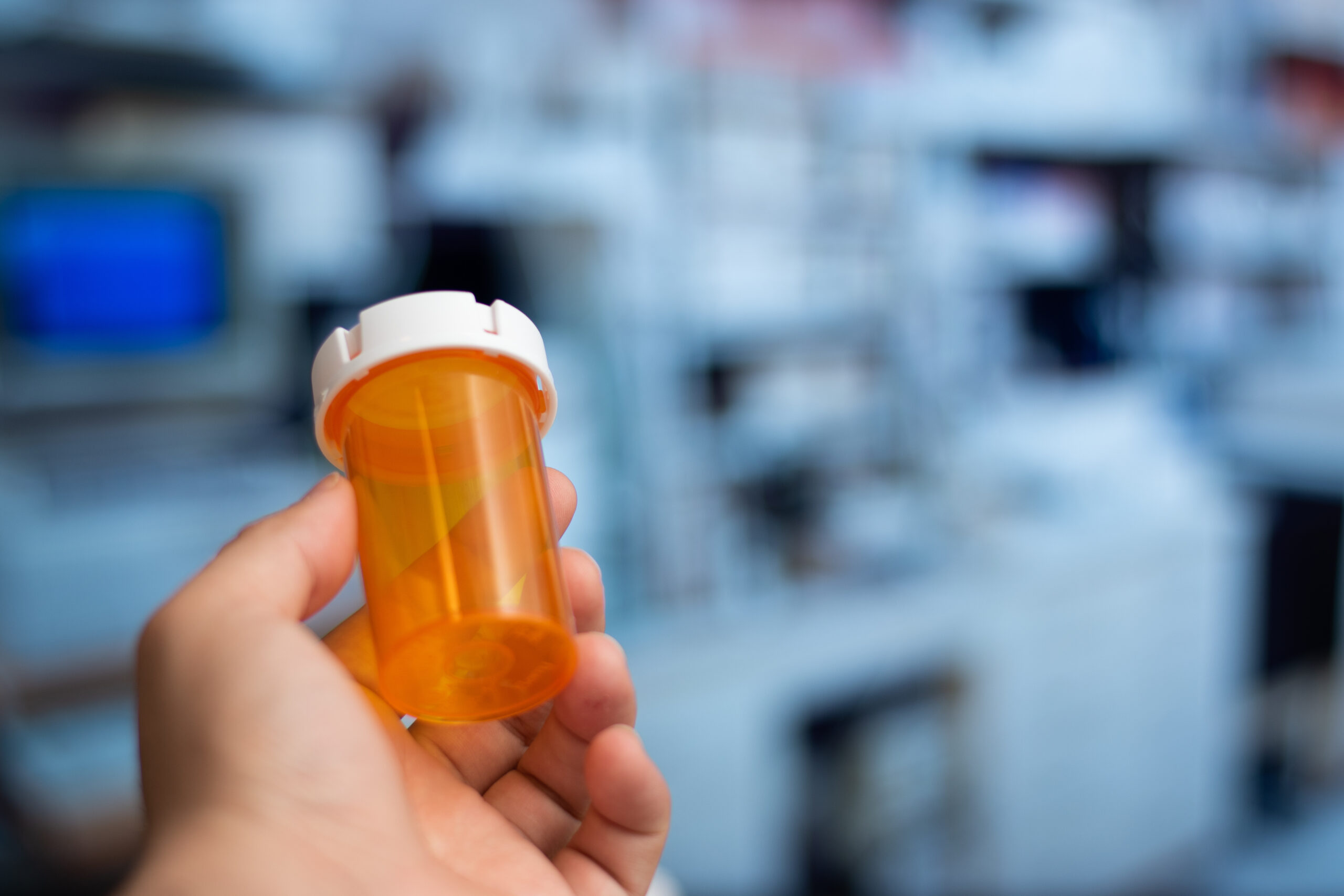 Hand holding an empty orange bottle of medicine in laboratory background